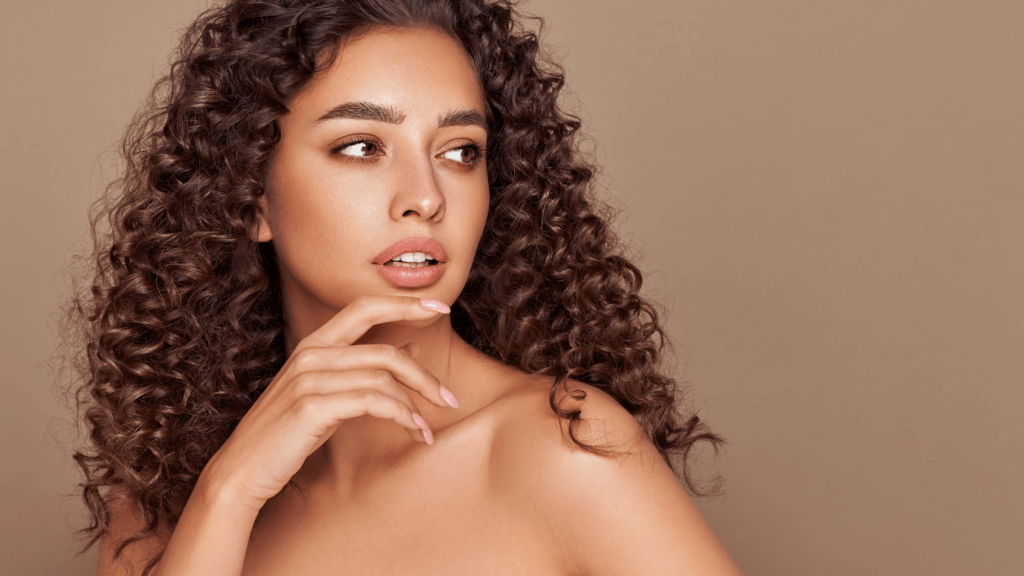 Portrait of a woman with radiant, healthy-looking skin, showcasing the results of a DiamondGlow treatment. She has luscious, curly brown hair that frames her face, emphasizing her glowing complexion and the rejuvenated appearance of her skin.