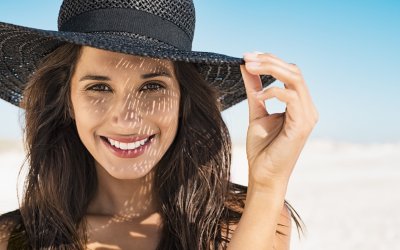 Portrait of beautiful young woman wearing summer black hat with large brim at beach. Closeup face of attractive girl with black straw hat. Happy latin woman smiling and looking at camera with sea in background.